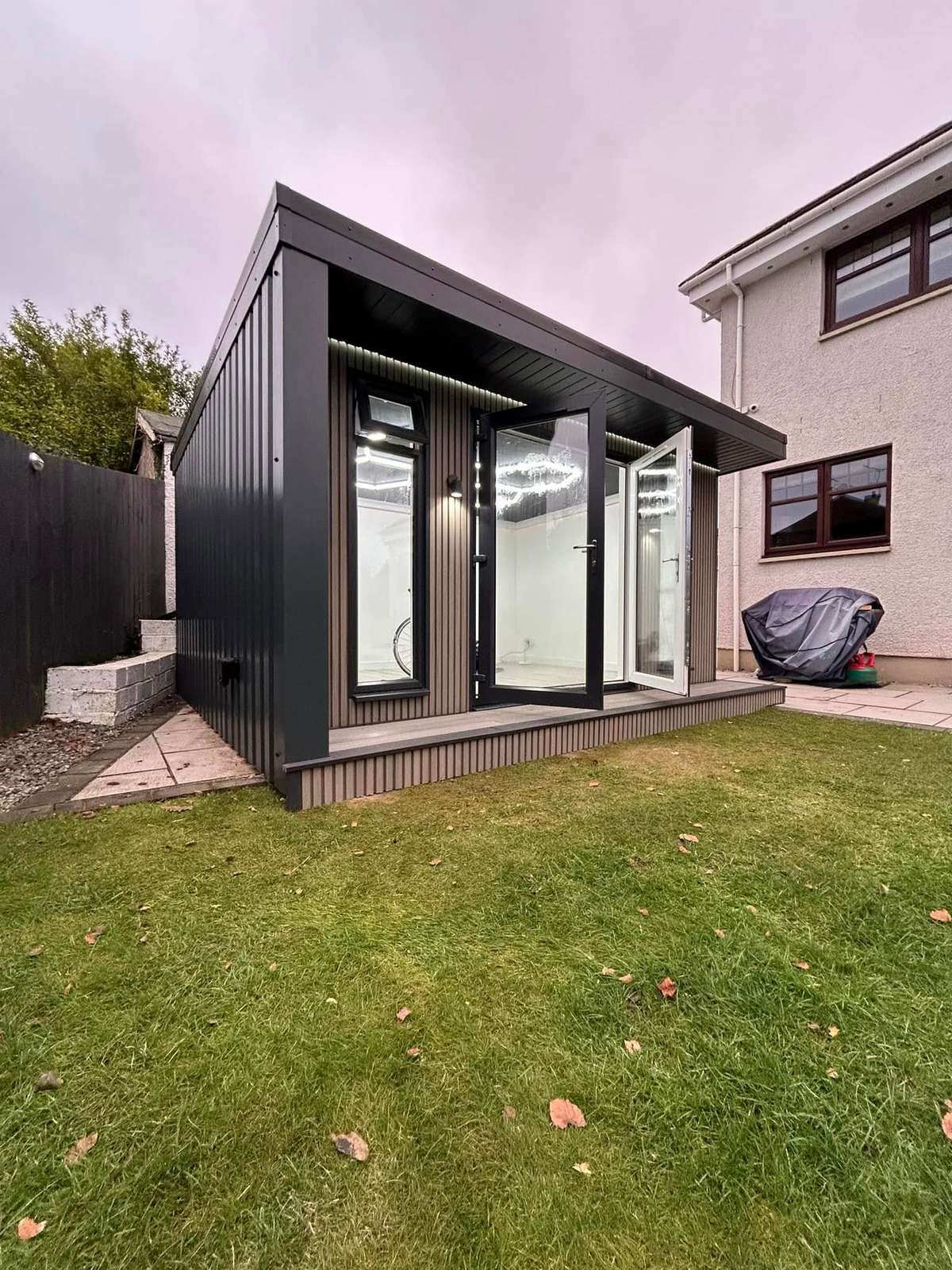 Dark clad garden cabin with a flat roof, standing on a lawn in daylight