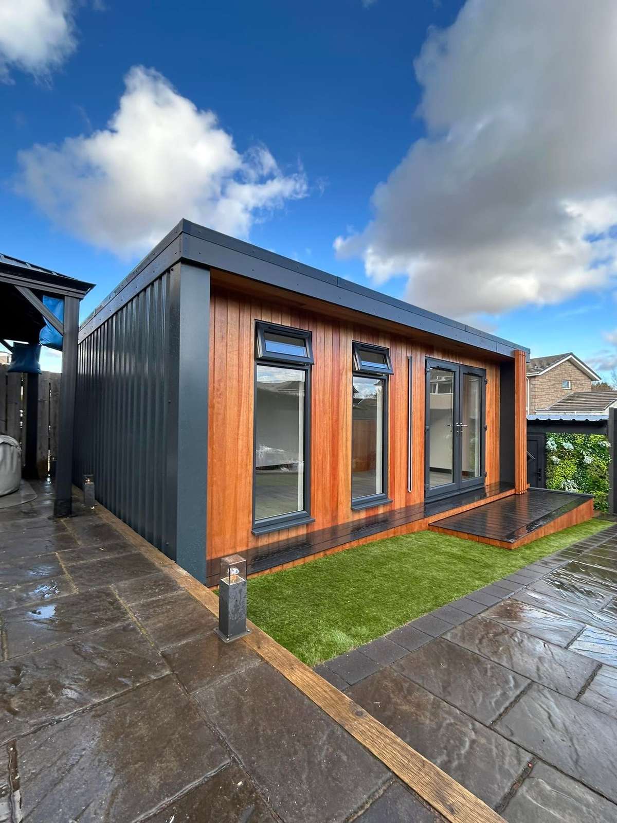 A dark clad cabin beside a timber clad cabin, in daylight