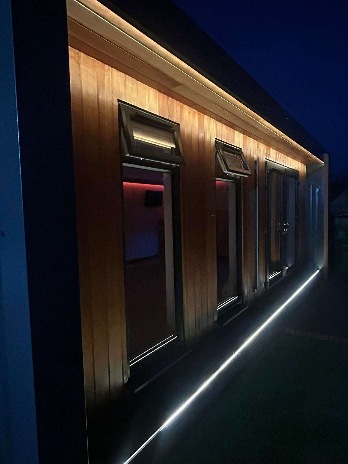 Timber clad cabin with LED light along the cladding, at night