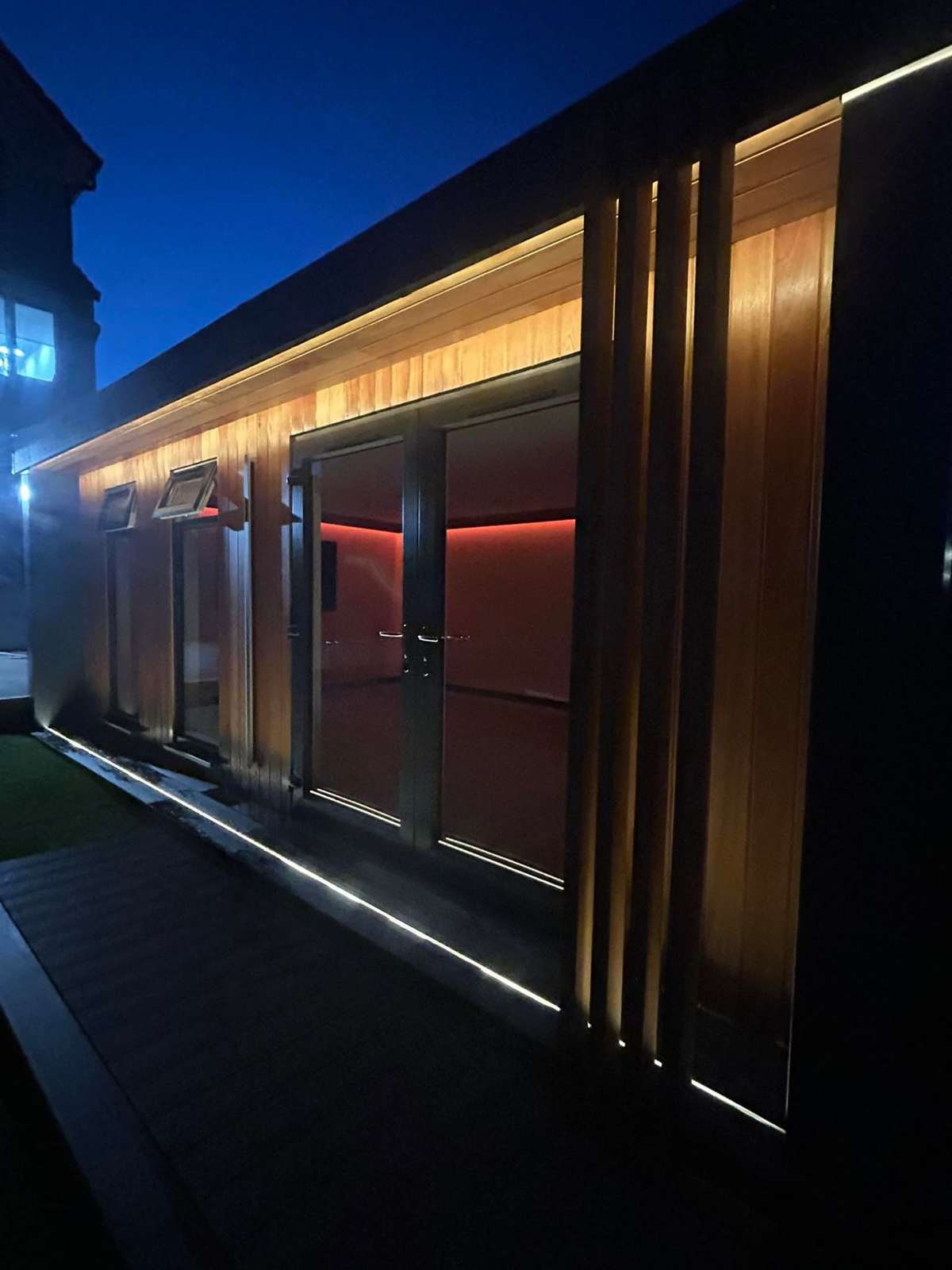 A long timber clad cabin with LED light, at night