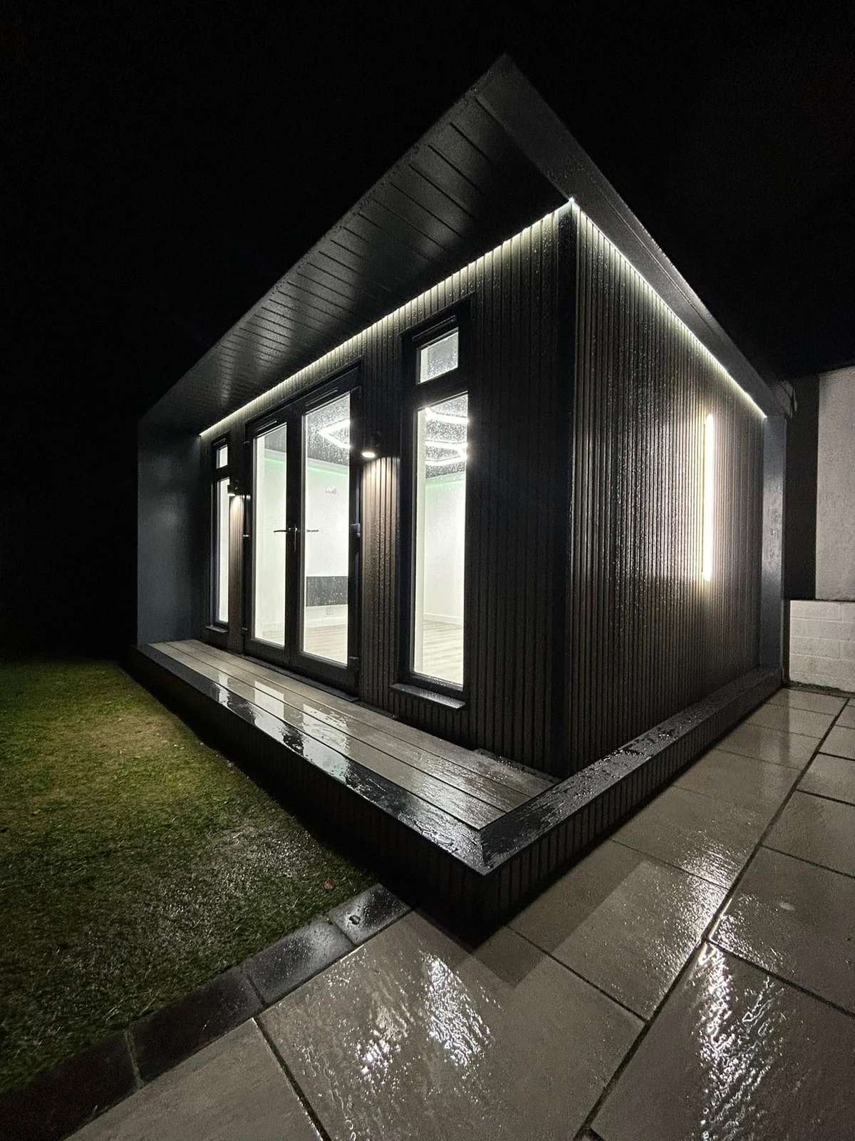 Dark clad cabin with a line of LED light under the eaves, at night