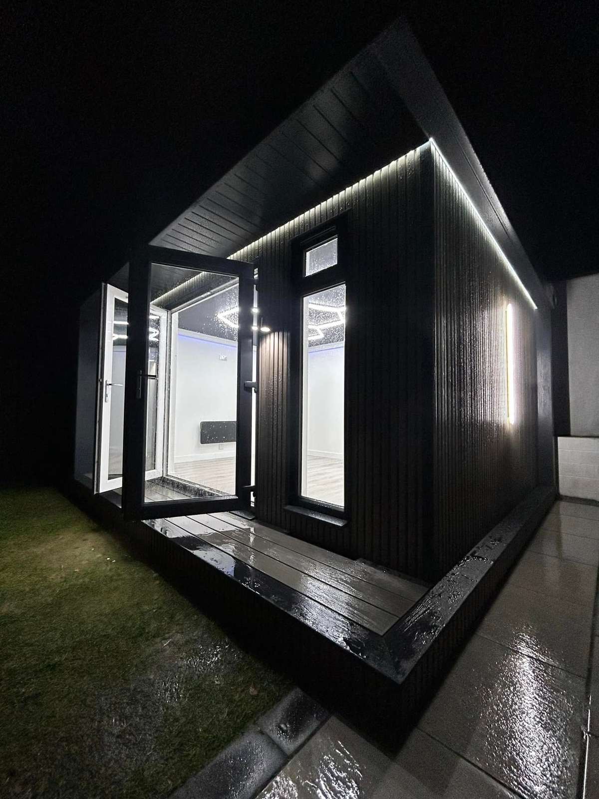 Dark clad cabin with a glass front, lit at night