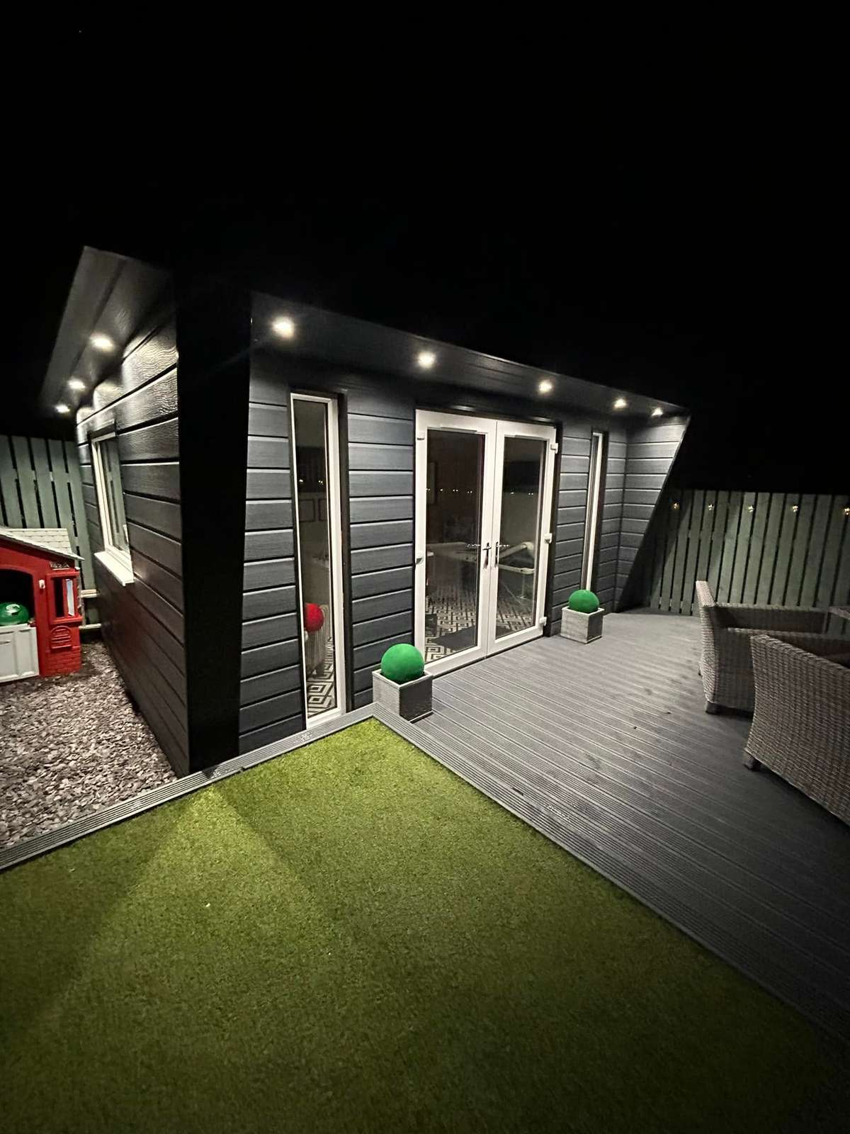 Garden room and decking at night, with grass in front